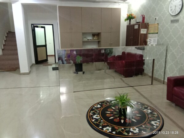 A spacious living area with a staircase, a reception desk, and a round table with a plant.