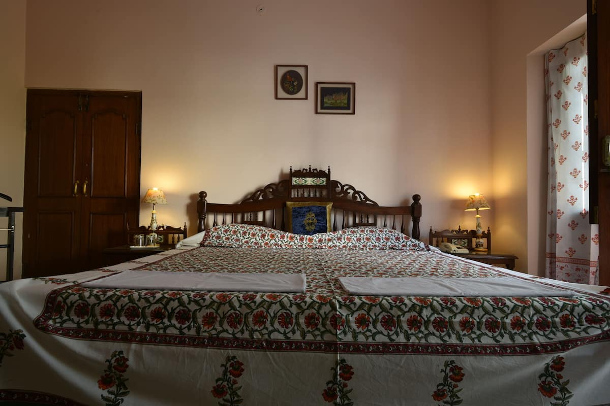 Une chambre à coucher avec un grand lit, une tête de lit en bois, deux tables de chevet avec des lampes, une armoire et deux tableaux encadrés accrochés au mur.