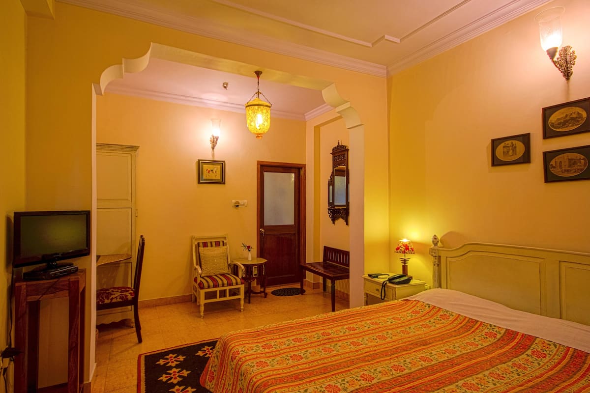 Une chambre d’hôtel avec un lit, une télévision, une chaise, une petite table et une lampe.