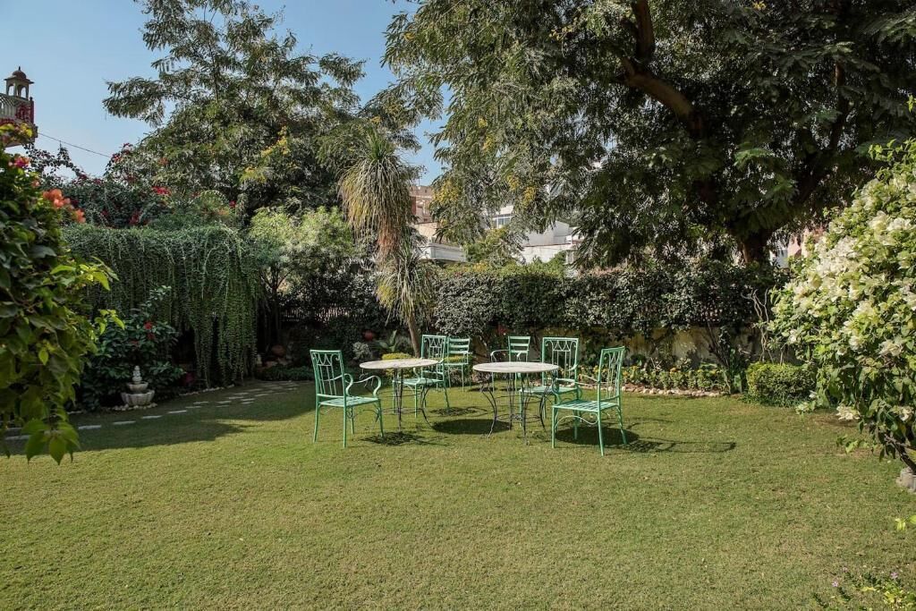 Un jardin bien entretenu, avec une pelouse, plusieurs chaises et tables en métal vert, disposées pour les repas en plein air.