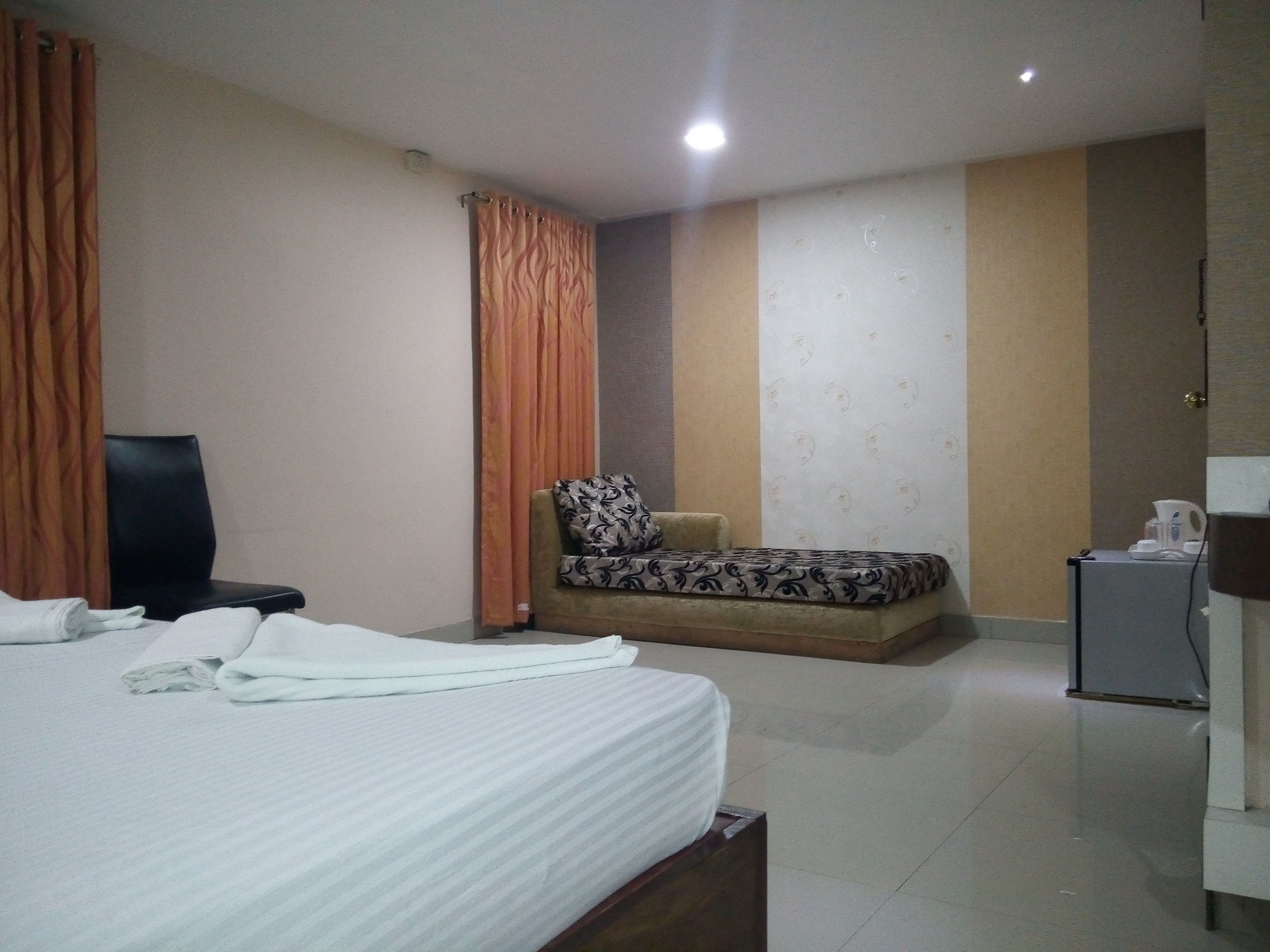 Una habitación de hotel con cama, sillón, sofá, cafetera y una pequeña mesa.