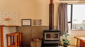 Una habitación con techo de madera, un ventanal grande, una cabeza de venado montada en la pared, un estufa de leña y vistas a la montaña desde la ventana.