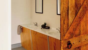 A bathroom with a wooden vanity, two sinks, a mirror, and a ceiling-mounted speaker.