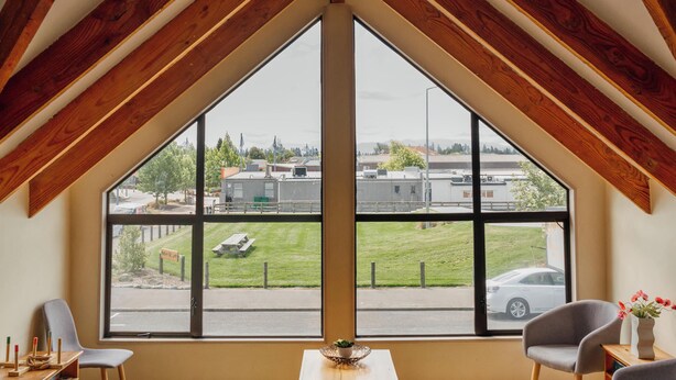 Una habitación con techo inclinado, ventanas amplias, un sofá de cuero y una mesa de madera.