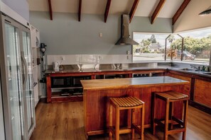 A modern kitchen with wooden bar stools, a large island, and a view of the neighborhood. - Snow Denn Lodge (Methven)
