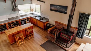 Una cocina moderna con una isla central, taburetes de madera, chimenea de ladrillo y un ventanal grande.