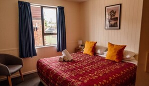 A hotel room with a large bed, two pillows, a chair, a window with curtains, a bedside table with a lamp, and a framed picture on the wall. - Snow Denn Lodge (Methven)