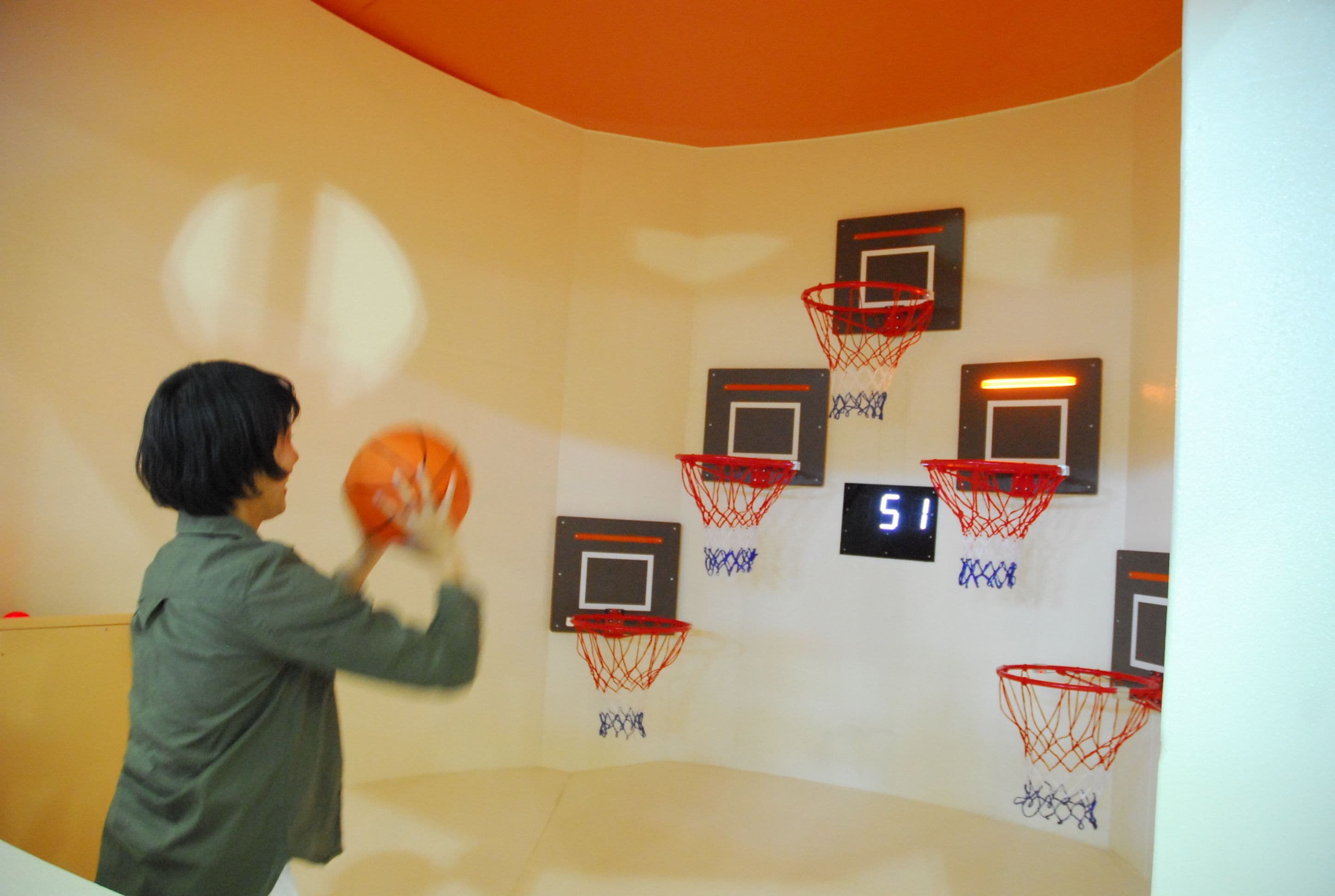 Una persona juega al baloncesto en una habitación con varios aros de baloncesto fijados en la pared.