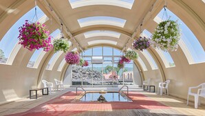 A sunlit indoor pool area with a view of a rocky landscape and a building in the background.