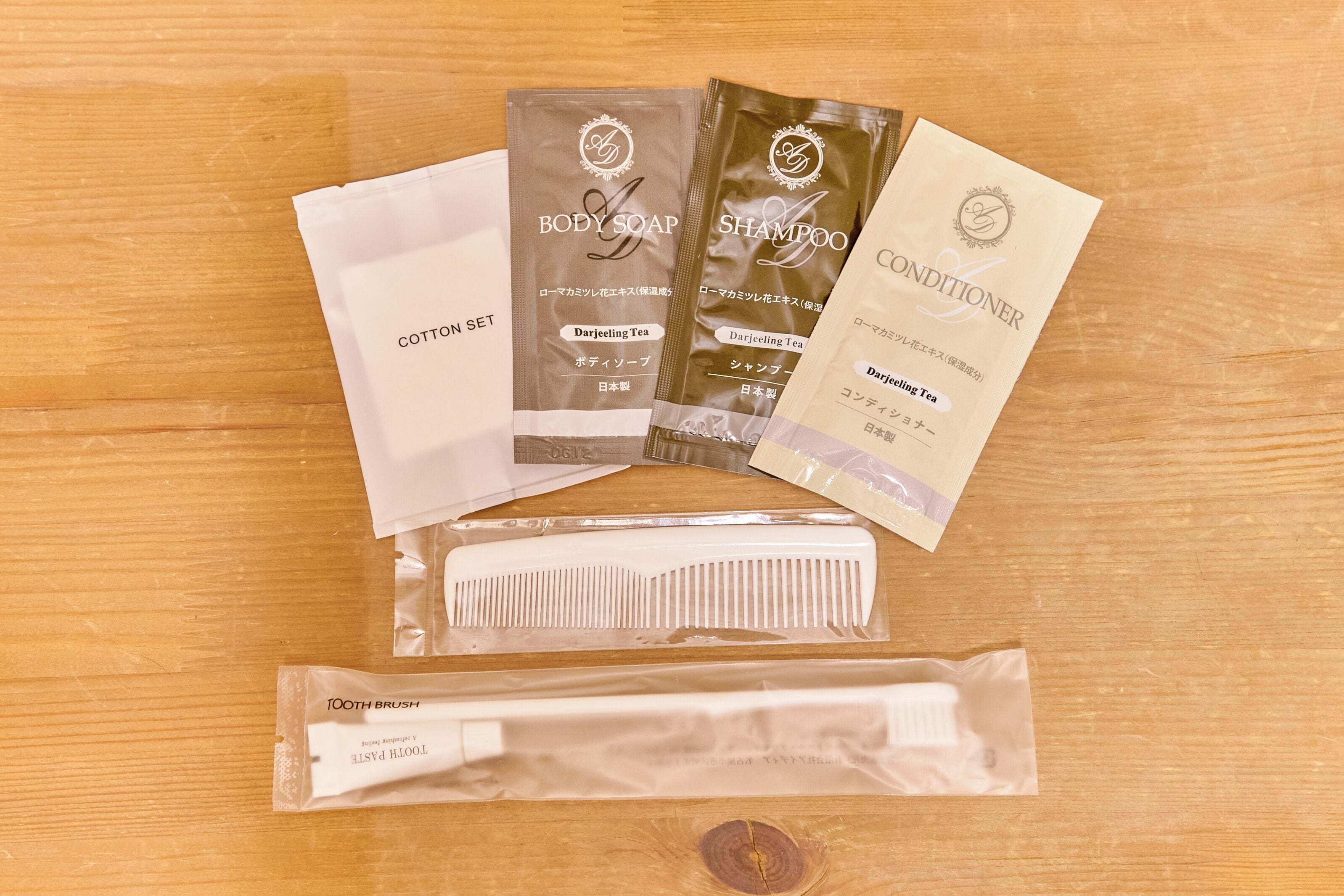 A wooden surface with various personal care items including body soap, shampoo, conditioner, a cotton set, a tooth brush, and a tool kit.