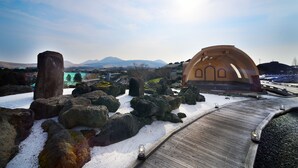Paisaje nevado con rocas grandes, un sendero de madera y un edificio en forma de cúpula.