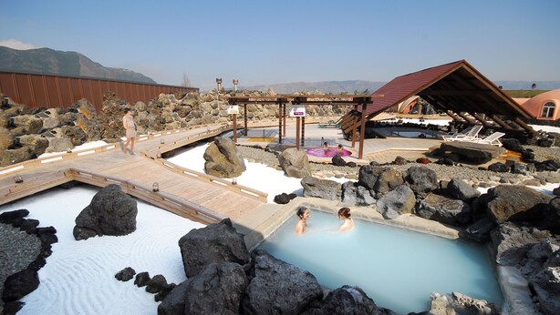 Un área de aguas termales con una terraza de madera, una piscina pequeña y una zona cubierta para sentarse.