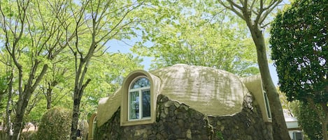 Ein Haus aus Stein mit Runddach und Fenster, umgeben von Bäumen.