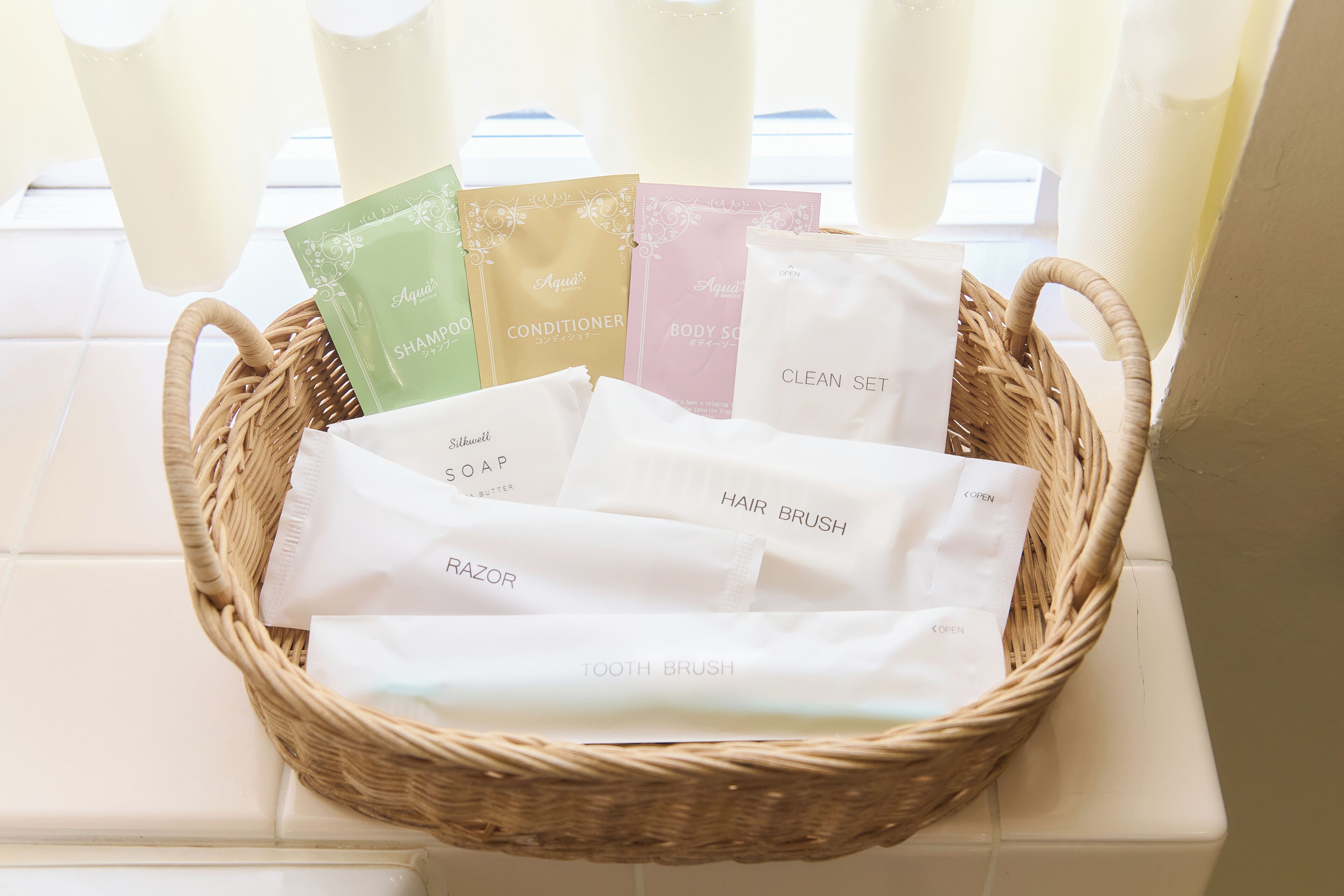 A wicker basket containing various toiletries including shampoo, conditioner, body soap, hair brush, razor, and tooth brush.