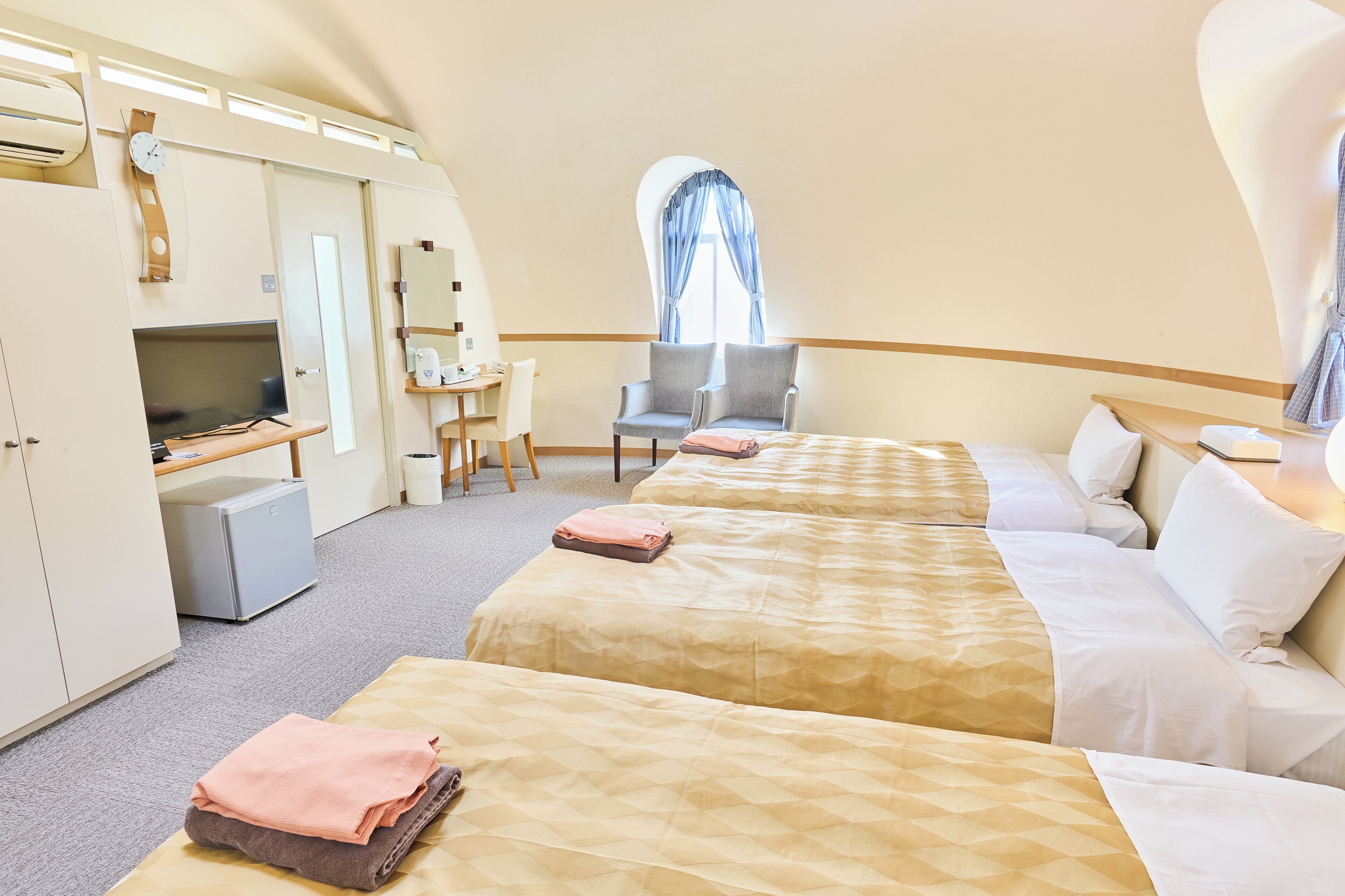 A hotel room with two beds, a desk with a computer, a chair, and a window with curtains.