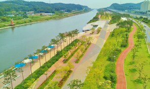 A riverside walkway with benches and trees, a bridge in the distance, and a road parallel to the river. - Good Moments sharehouse (Incheon)
