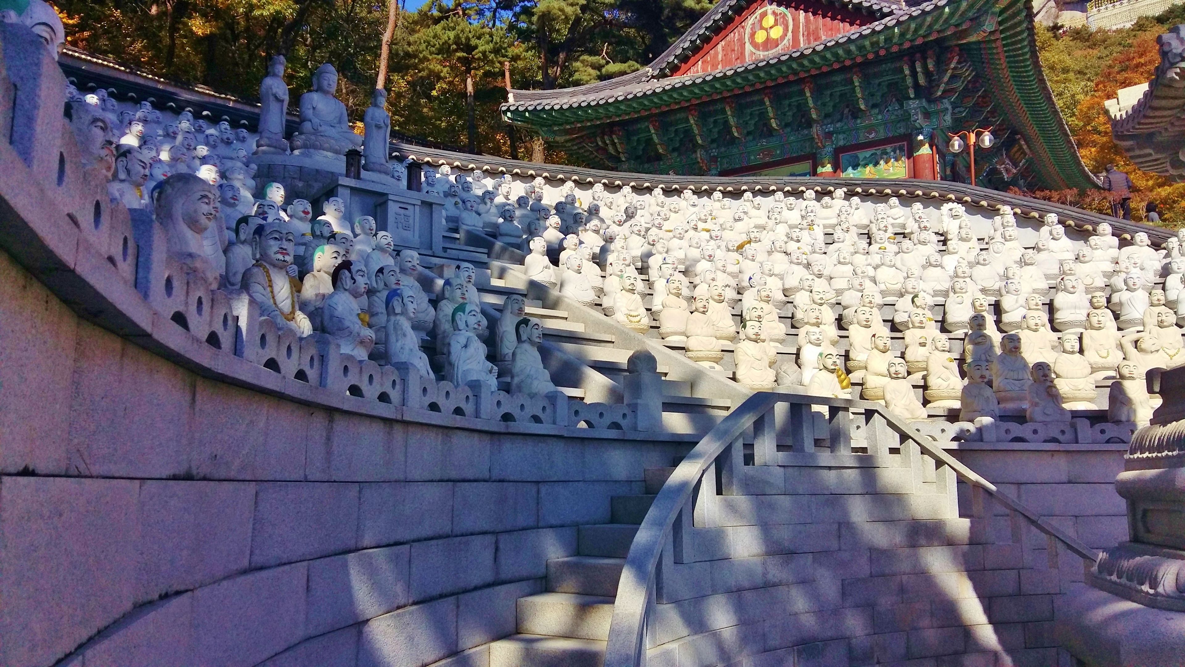 A large number of white stone statues arranged in tiers, with a traditional building in the background.