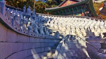 A large number of white stone statues arranged in tiers, with a traditional building in the background.