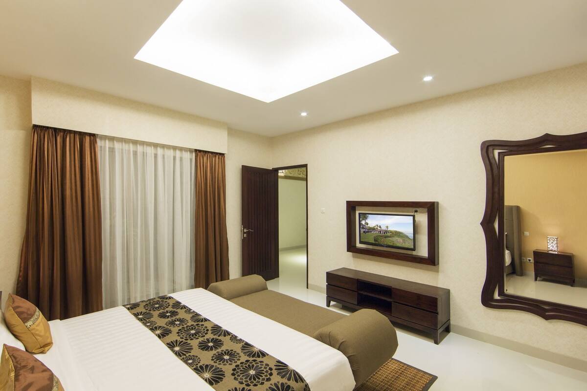 A hotel room with a large bed, a TV, a mirror, and a desk.