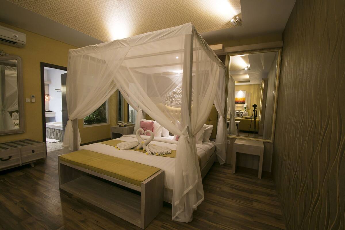A bedroom with a four-poster bed, a bedside table, a mirror, and a wooden floor.