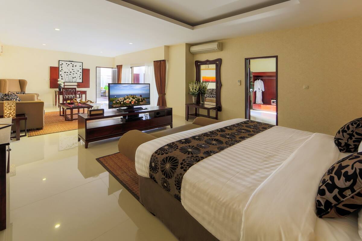 A modern hotel room with a large bed, a TV, a desk, and a seating area.