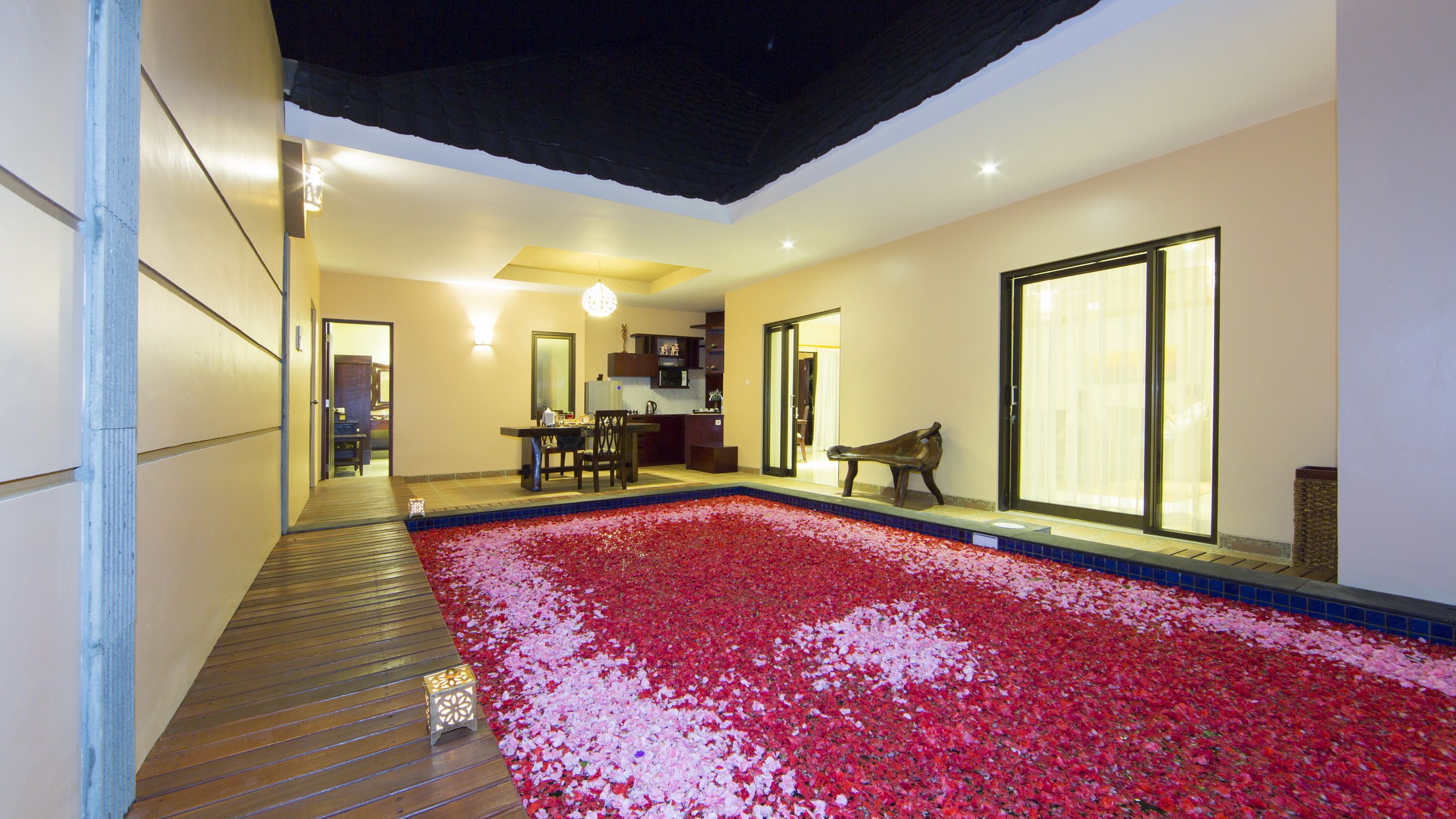 Un'ampia area interna con piscina ricoperta di petali di rosa, un pontile in legno e un angolo relax con una panca.