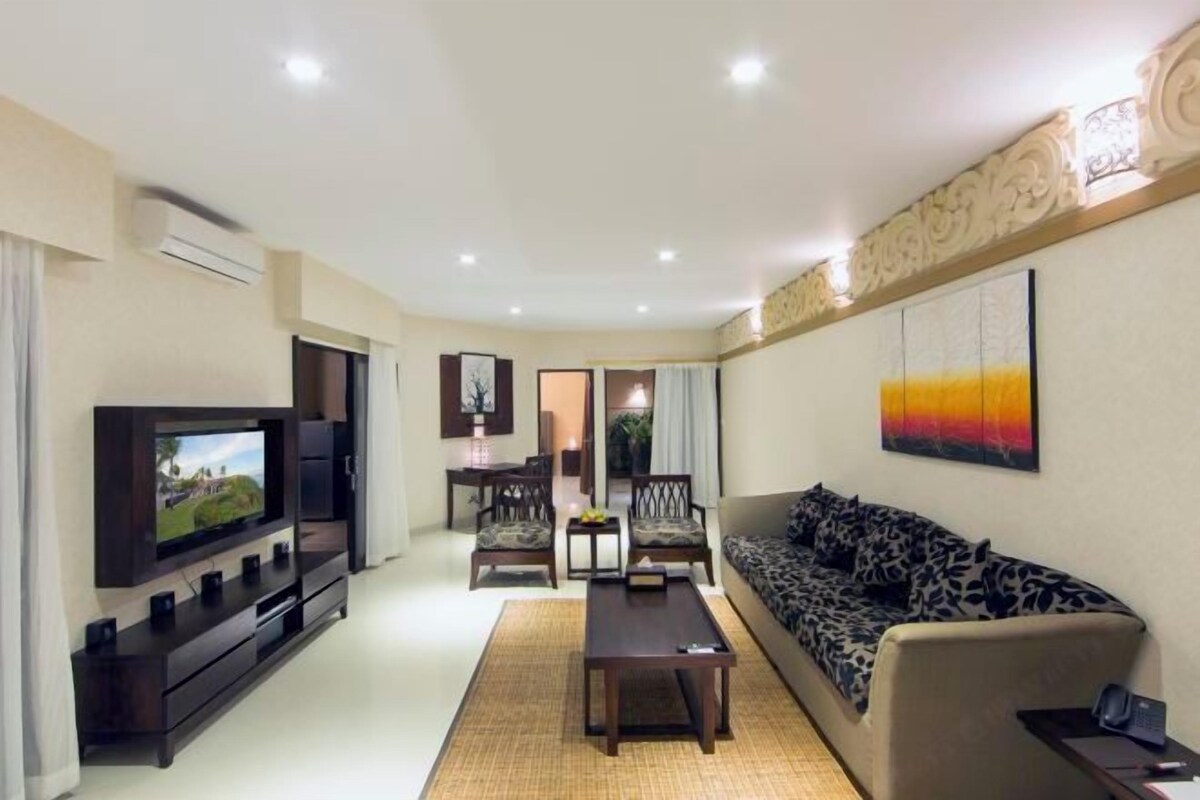 A modern living room with a flat-screen TV, dark wooden entertainment unit, patterned sofa, and a dining area with chairs and a table.