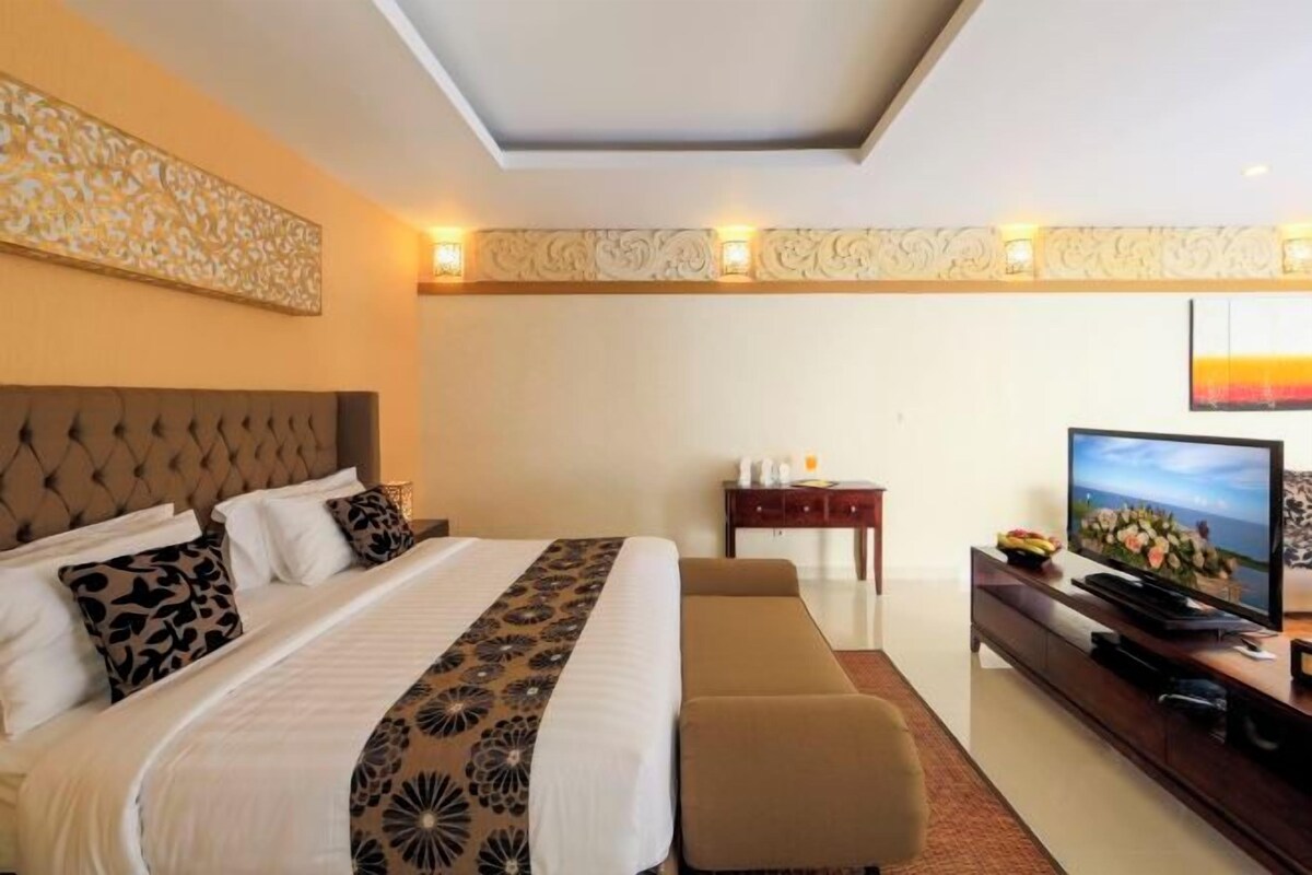 A hotel room with a large bed, a TV, a small table, and a decorative wall panel.