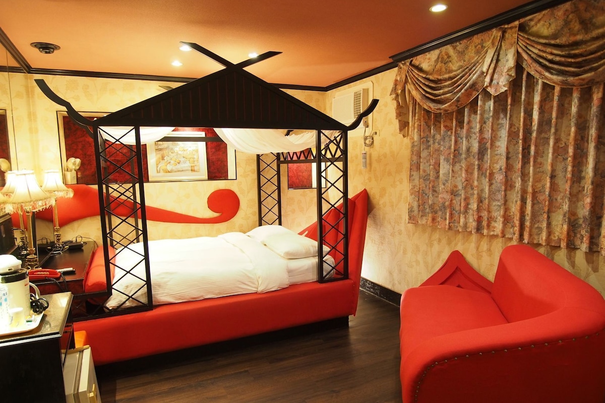 Una habitación con cama con dosel, un sillón rojo, un escritorio con lámpara y un aire acondicionado de pared.