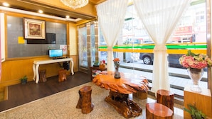 A reception area with a wooden reception desk, a computer monitor, a chandelier, and a large window with curtains. - Day Chen Hotel (Yilan)