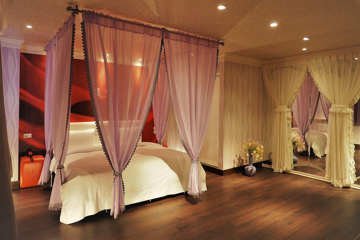 Una cama con dosel y cuatro columnas, un espejo y un florero con flores.