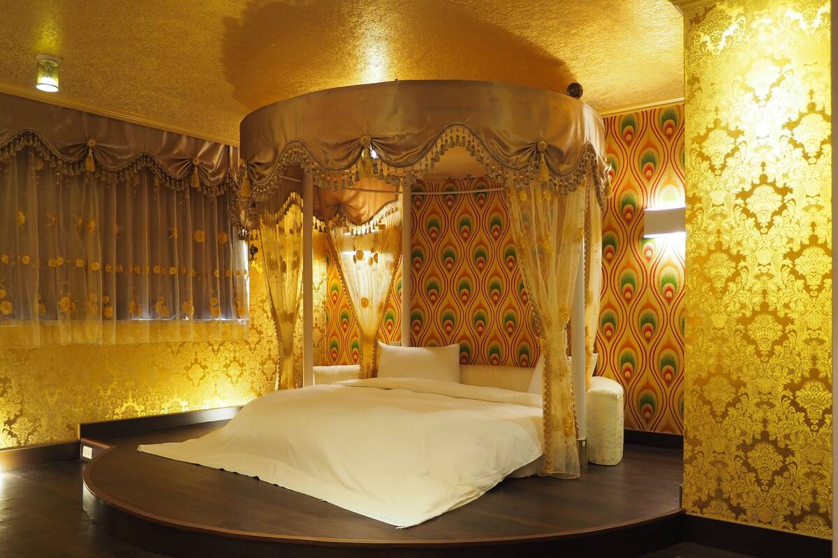 Una cama con dosel en un cuarto con papel tapiz ornamentado y una plataforma redonda de madera.