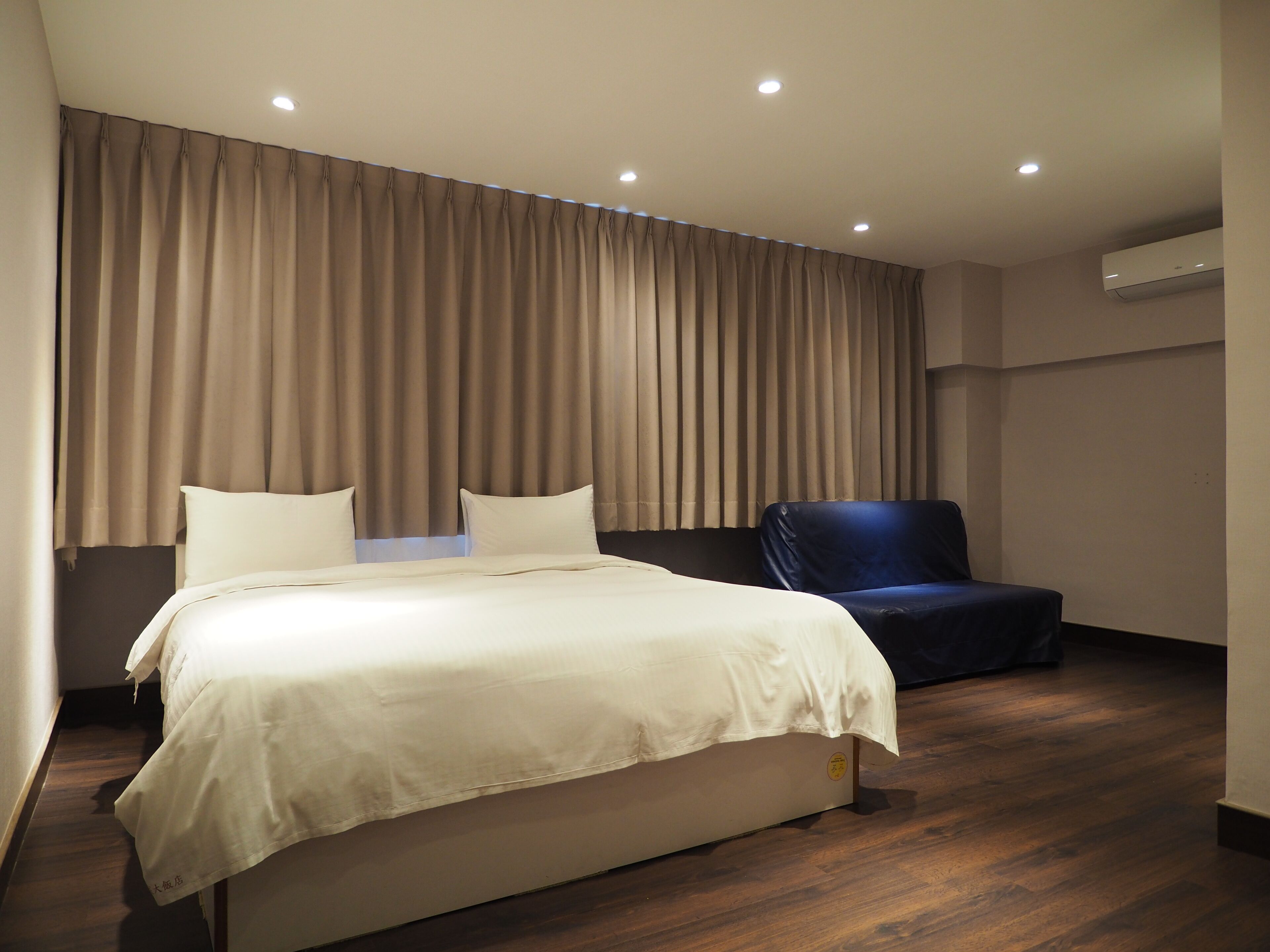 Una camera d'albergo moderna con un letto grande, una poltrona blu scuro e un'ampia finestra con tende.