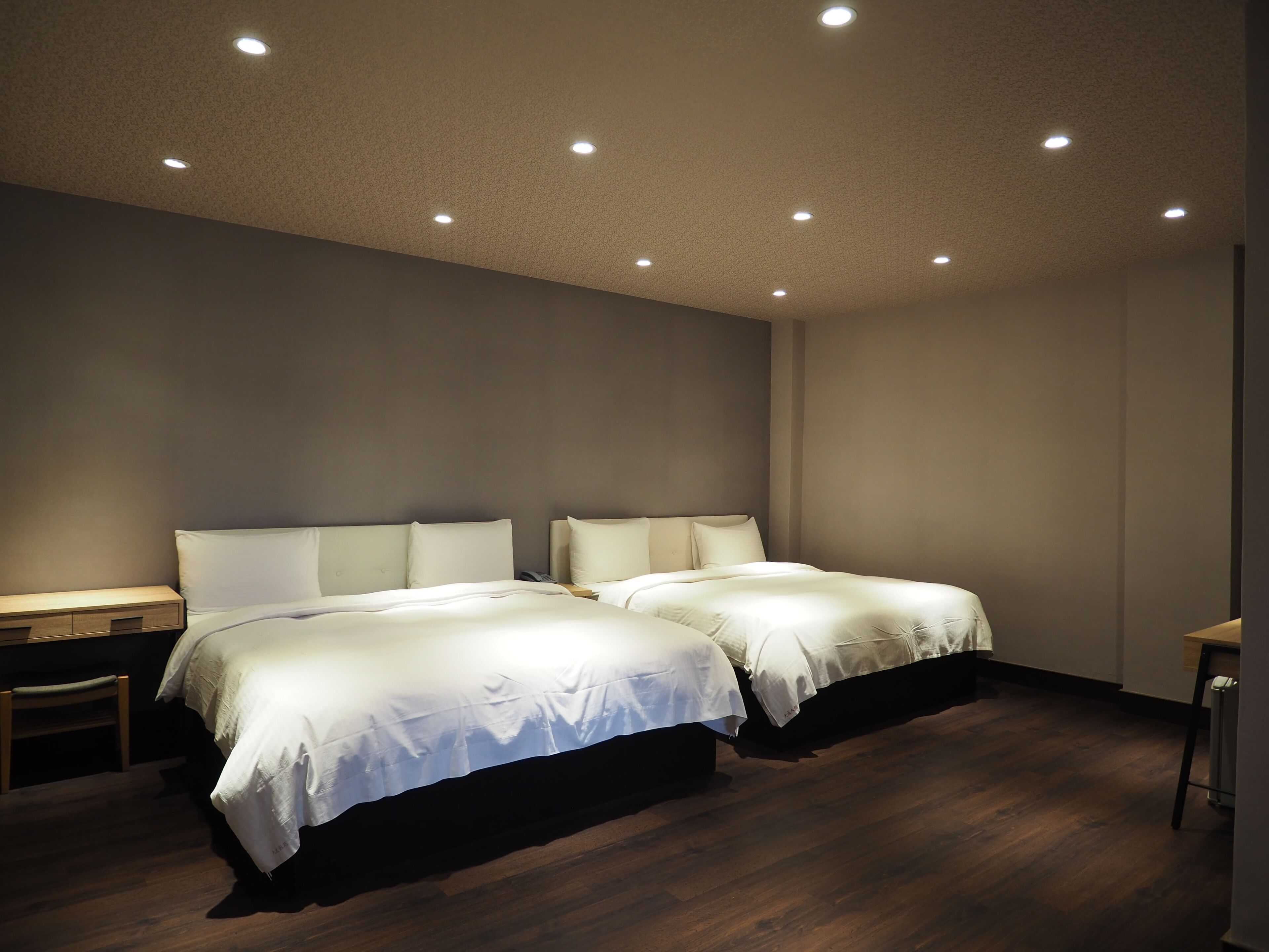 A hotel room with two beds, a desk, and a chair.