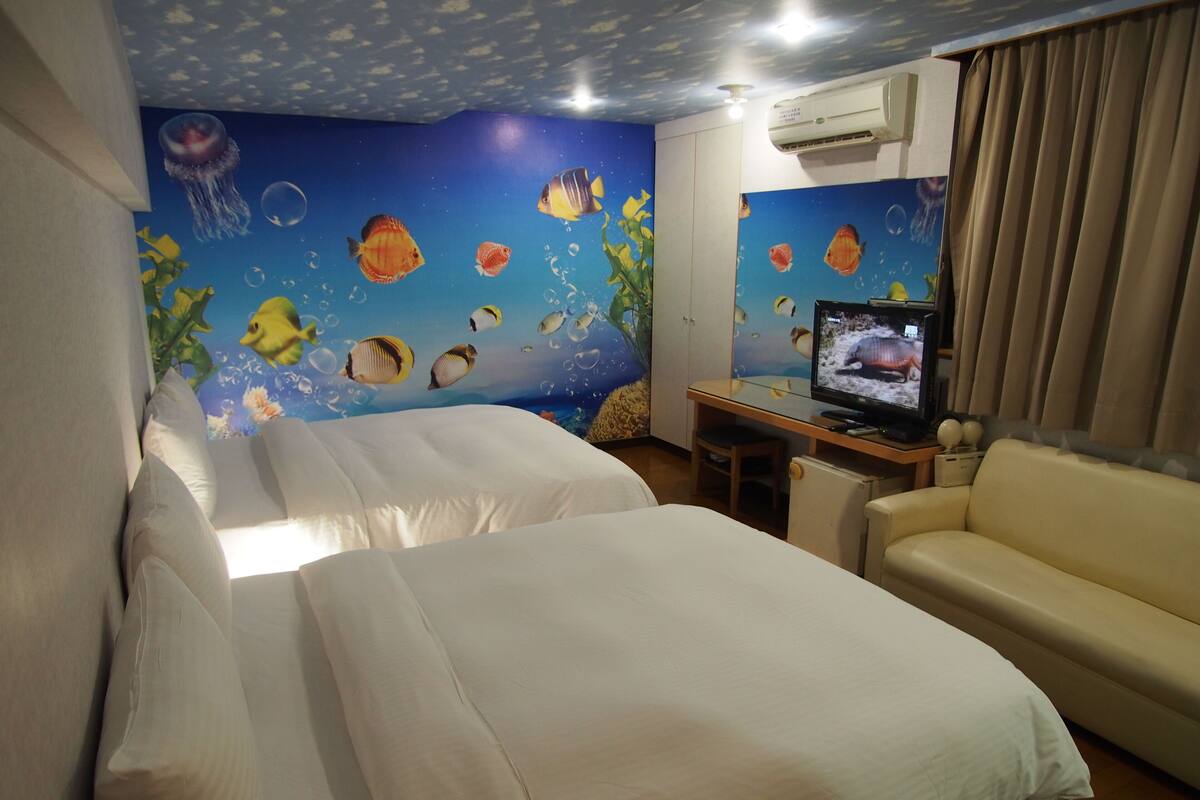 Habitación de hotel con dos camas, televisión, escritorio y sofá.