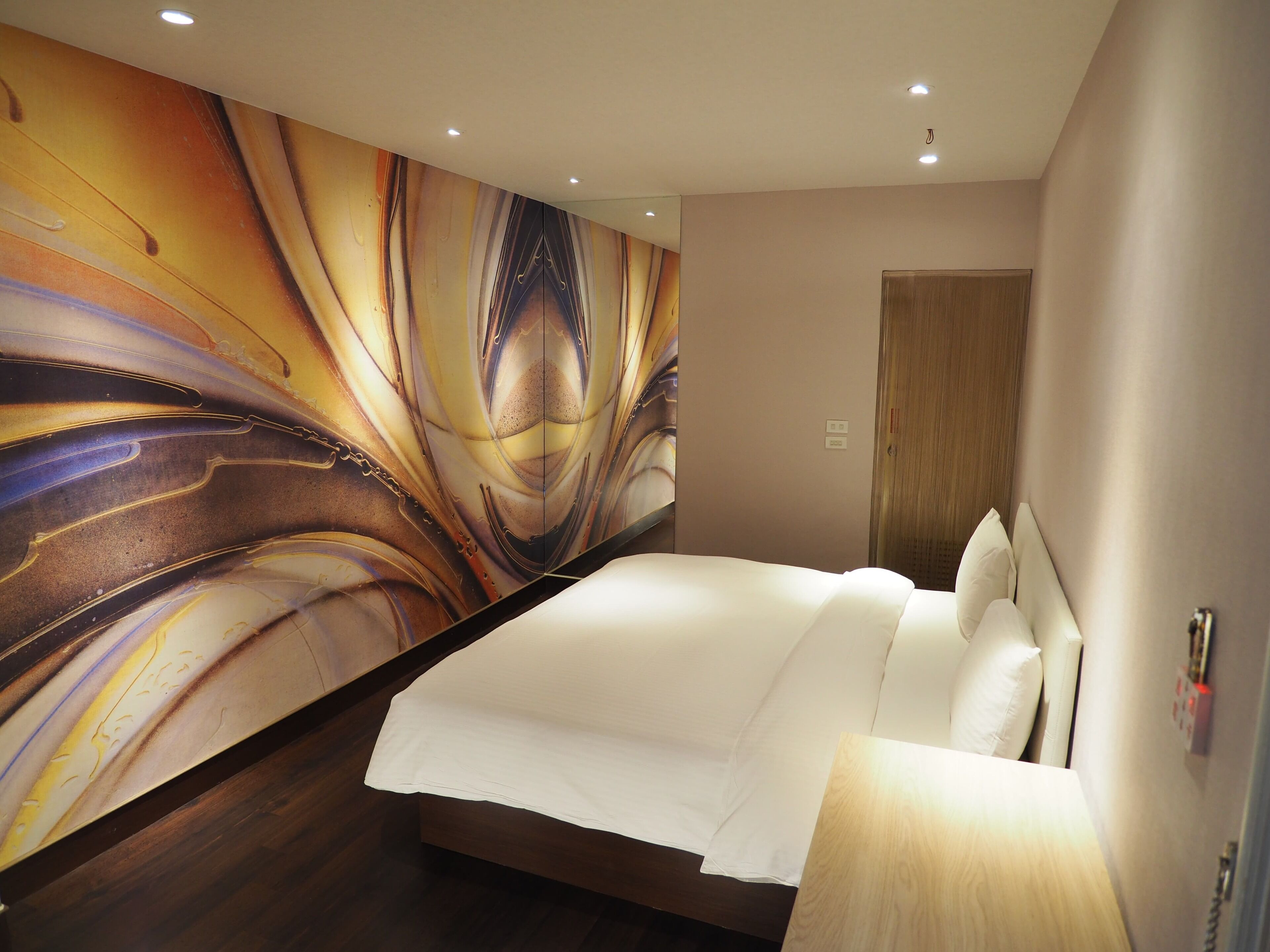 A hotel room with a large abstract mural on the wall, a neatly made bed, and a wooden door.