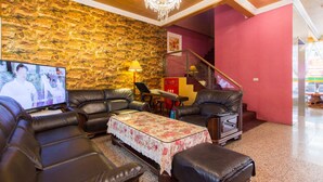 A living room with a stone wall, leather furniture, a chandelier, and a television. - Day Chen Hotel (Yilan)