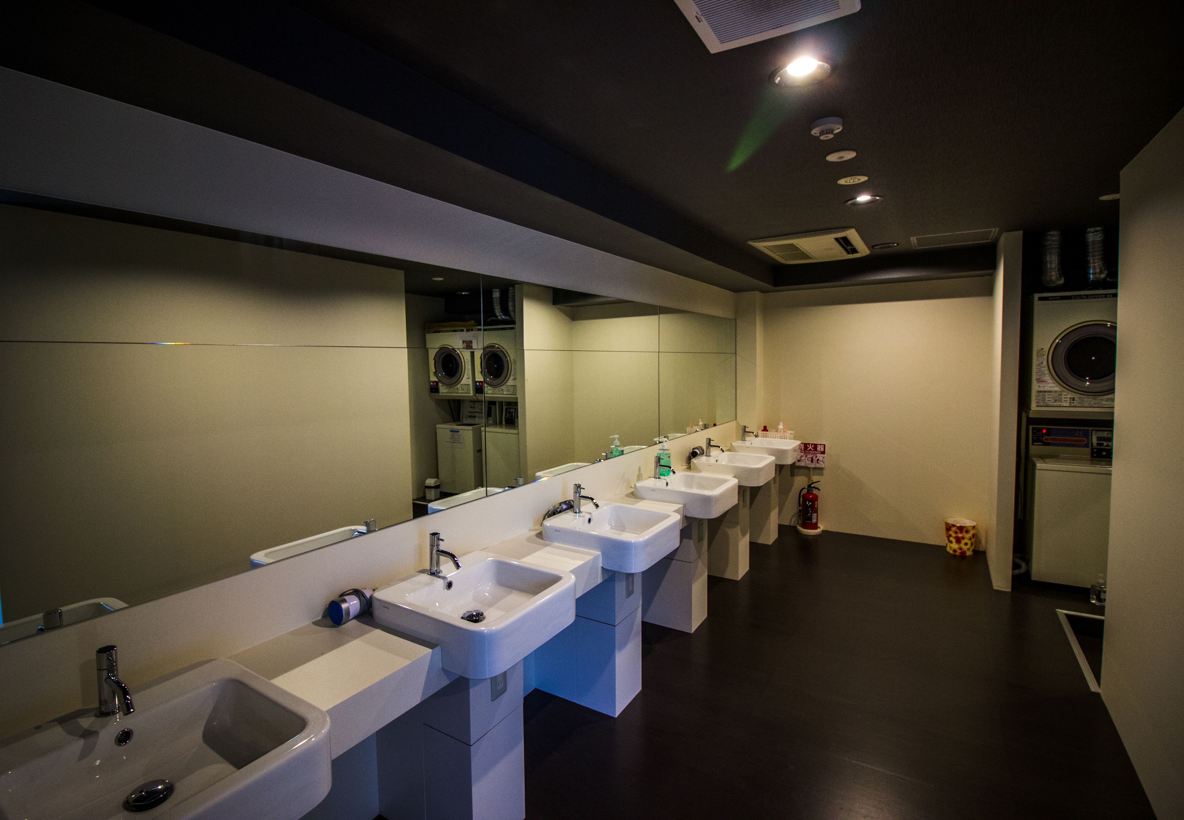 A row of sinks with mirrors, a washing machine, and a fire extinguisher in a public restroom.