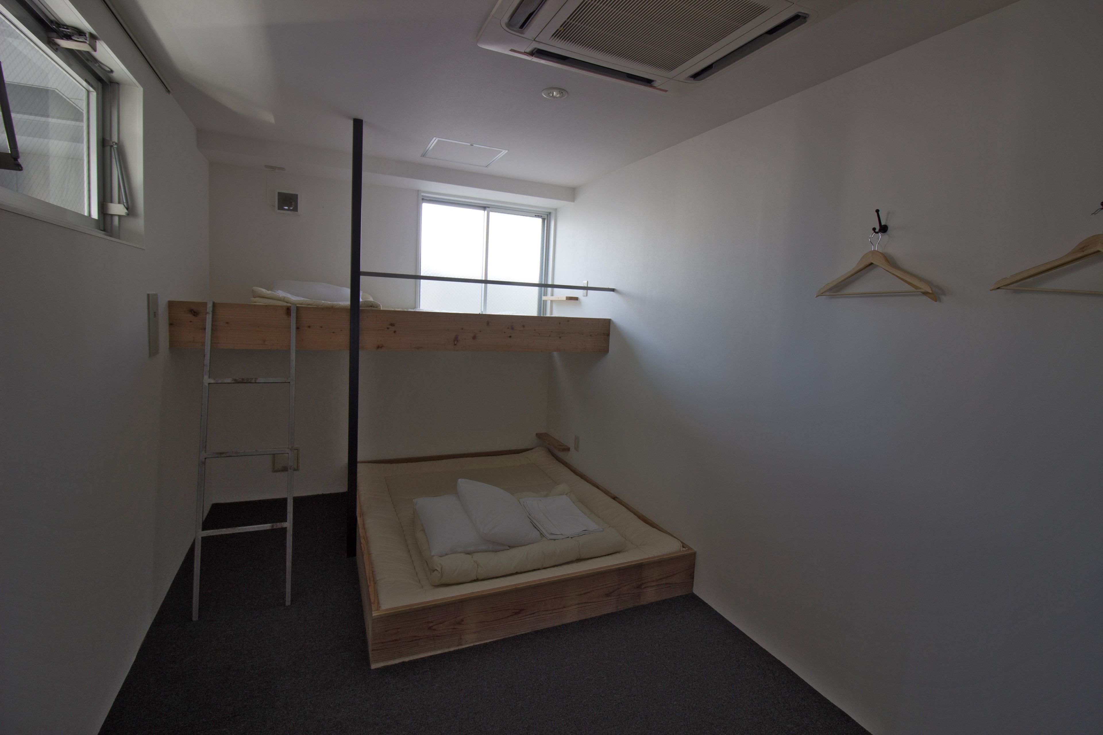 A small, minimalist bedroom with a bunk bed, a ladder, a window, and a wall-mounted hanger.