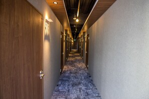 A hotel hallway with wooden doors, a patterned carpet, and recessed lighting. - Santiago Guesthouse Hiroshima – Hostel (Hiroshima)