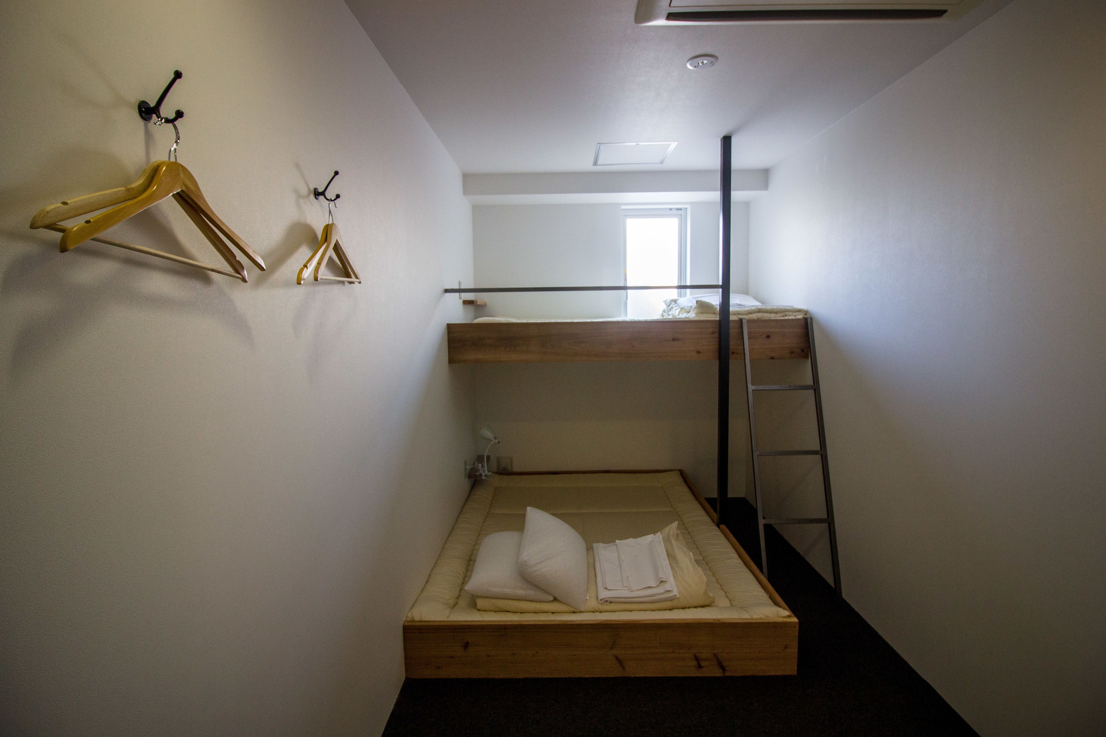 A bunk bed room with a wooden ladder, a small window, and two wooden hangers on the wall.