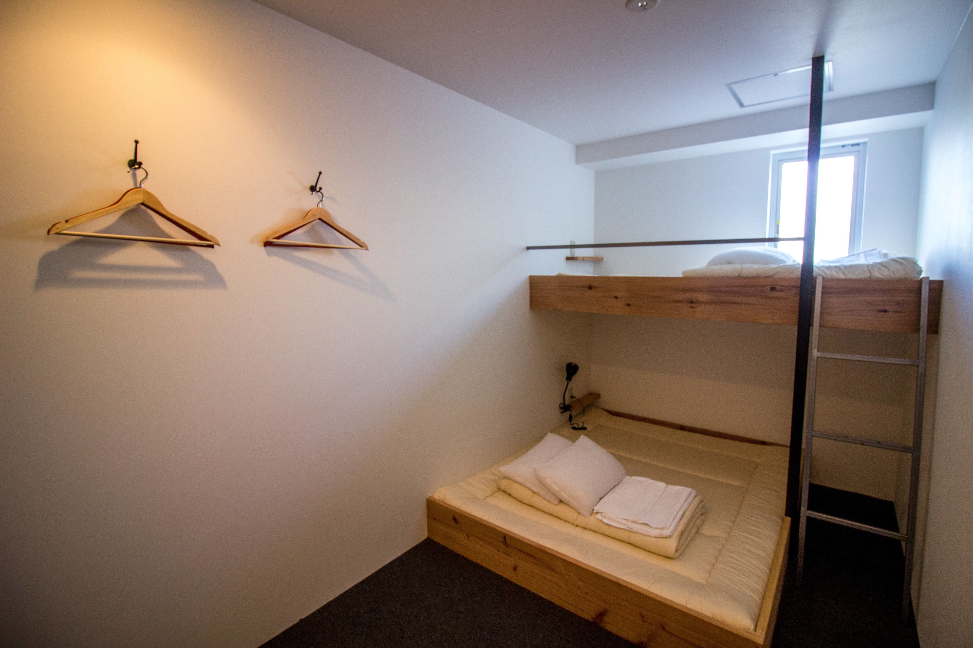 Un lit superposé avec une échelle en bois, un lit simple en dessous et deux cintres en bois fixés au mur.