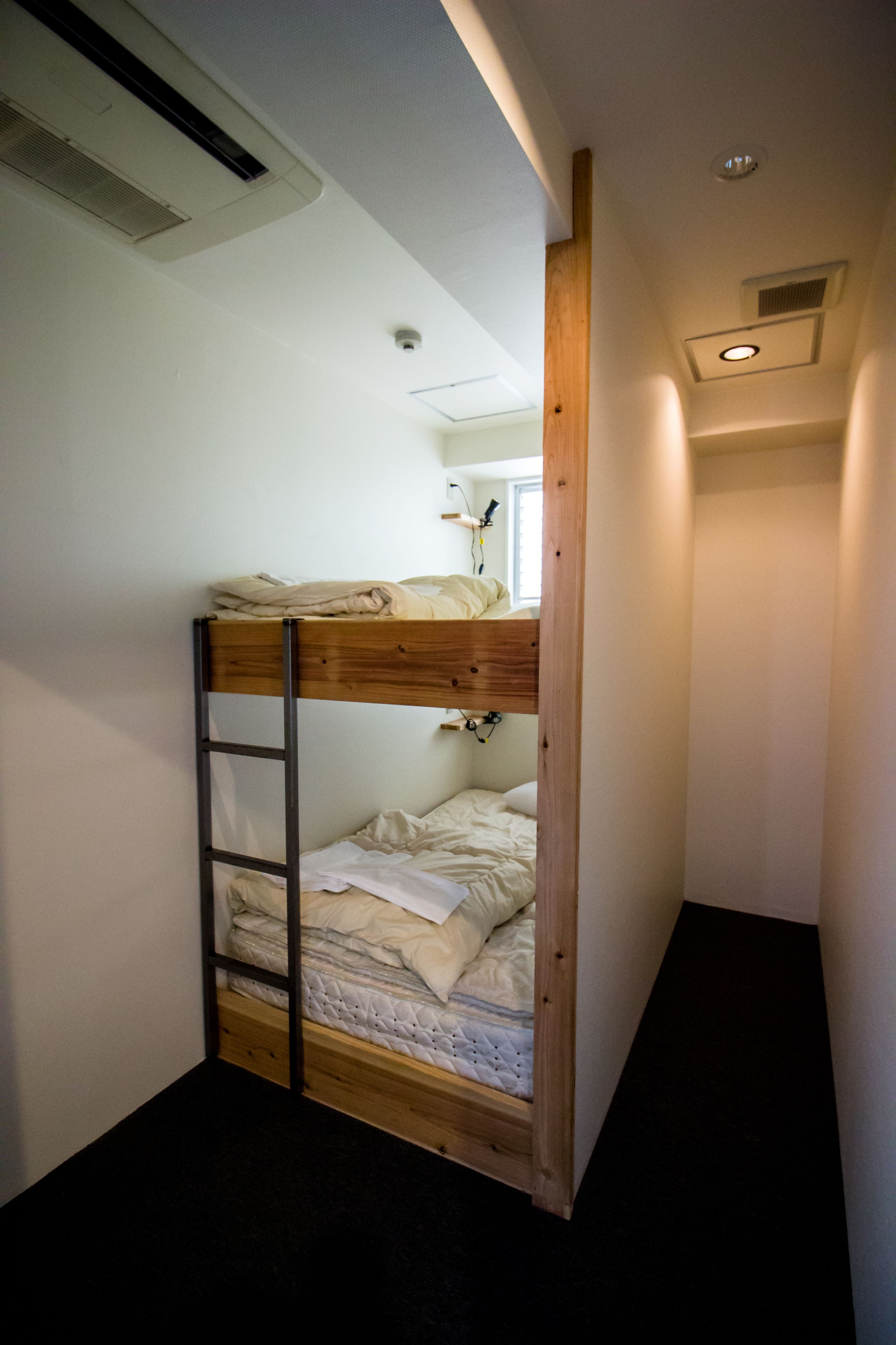 A bunk bed in a narrow room with a ladder, a window, and a ceiling vent.