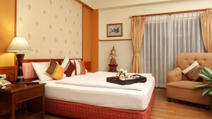 Habitación de hotel con cama, una silla, mesita de noche, lámpara, estatua, un cuadro en la pared y ventana con cortinas.