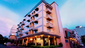 Un hotel de varios pisos con balcones, una entrada cubierta y un estacionamiento.