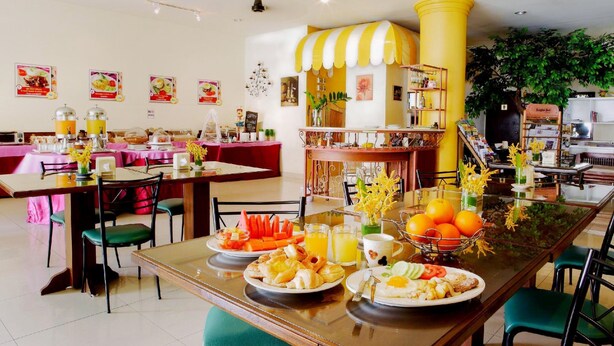 Comedor con mesas dispuestas para el desayuno, con platos de comida, bebidas y un toldo a rayas amarillas.