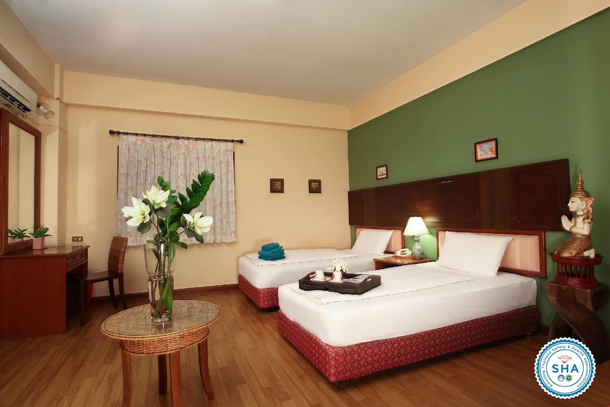 A hotel room with two beds, a dining table, a chair, a small table with a vase, and a decorative statue.