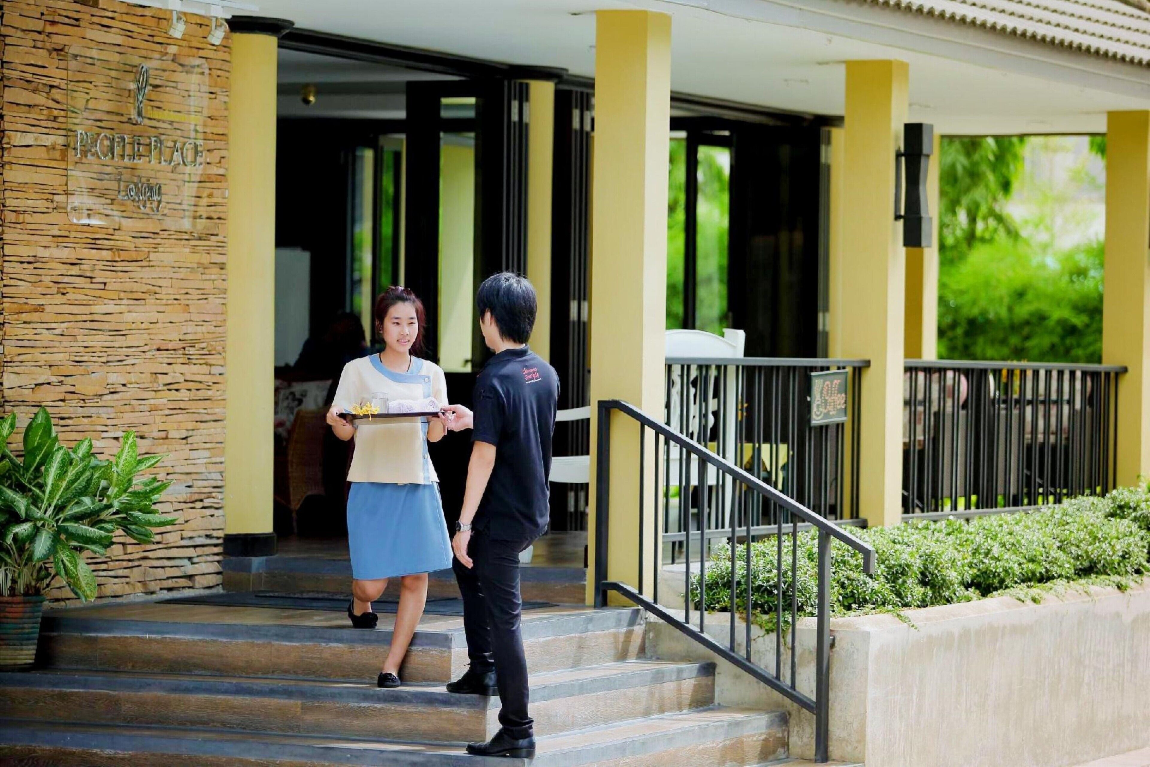 A hotel entrance with a stone facade, a staircase leading to the entrance, and a small garden area with a railing.