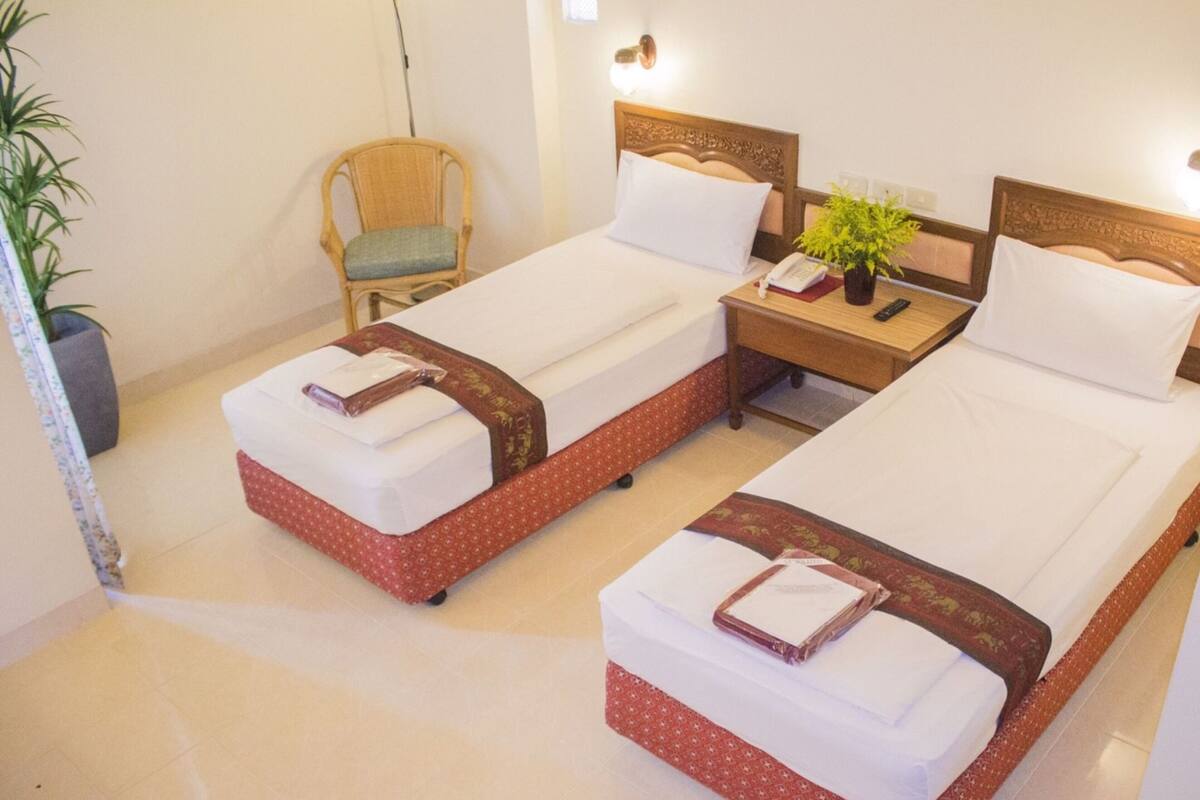 A hotel room with two single beds, a nightstand, a chair, and a potted plant.