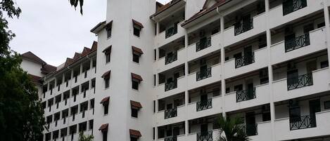 A multi-story hotel with a central tower, balconies, and a parking area.